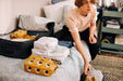 Person packing clothes into IKEA RENSARE packing cubes on a bed preparing for travel