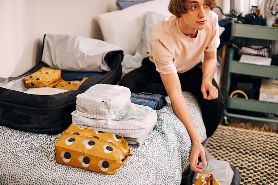 Person packing clothes into IKEA RENSARE packing cubes on a bed preparing for travel