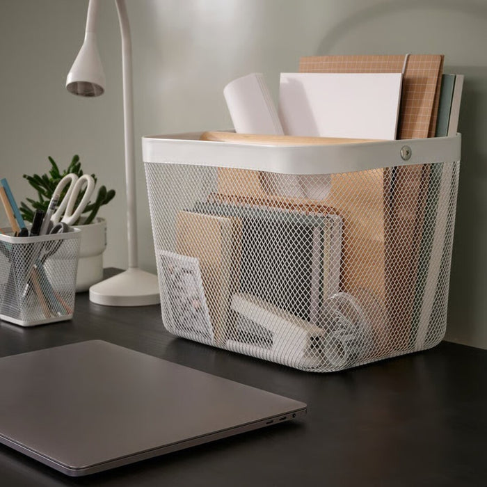 Mesh storage basket on a desk with office supplies, next to a laptop and lamp.