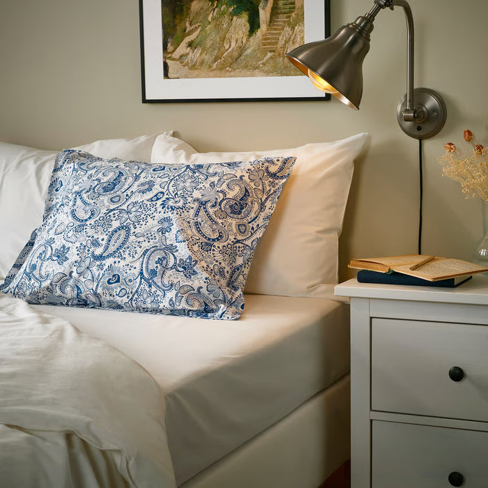IKEA RODGERSIA blue paisley pillowcase styled on cream bed with white bedside table flowers and lamp