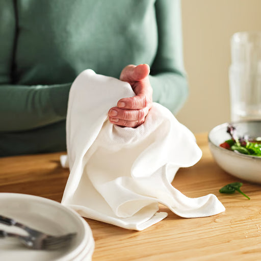 Person holding IKEA RÖDSPÄTTA white tea towel near kitchen table with bowls and utensils