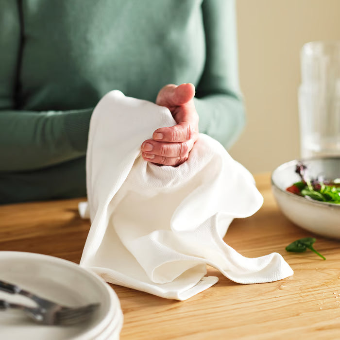 Person holding IKEA RÖDSPÄTTA white tea towel near kitchen table with bowls and utensils