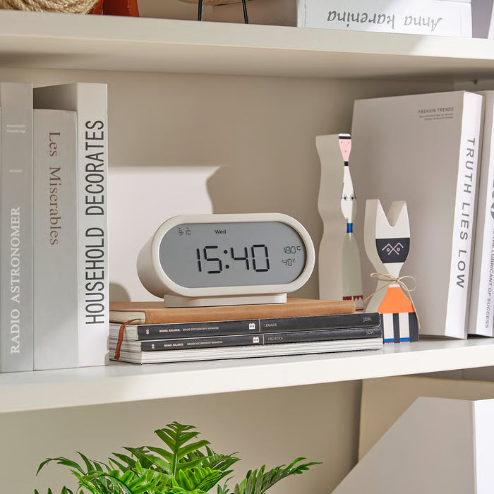 Digital clock on a shelf with books and decorative items