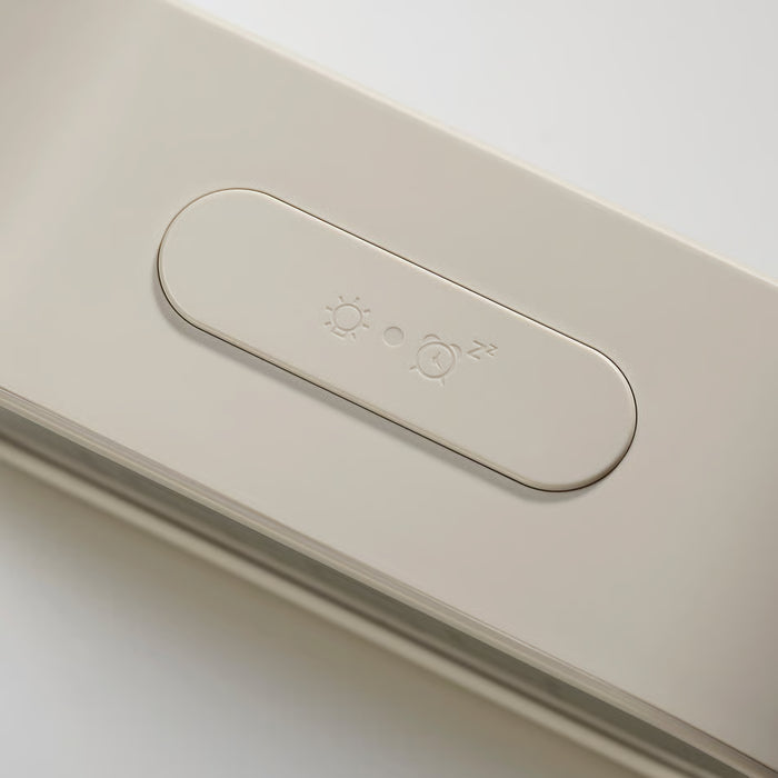 Close-up of a minimalist light switch panel with sun, moon, and alarm icons on a warm off-white surface.