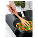 Hand using IKEA RÖRT wooden fork to stir vegetables in a black non-stick pan on a stove