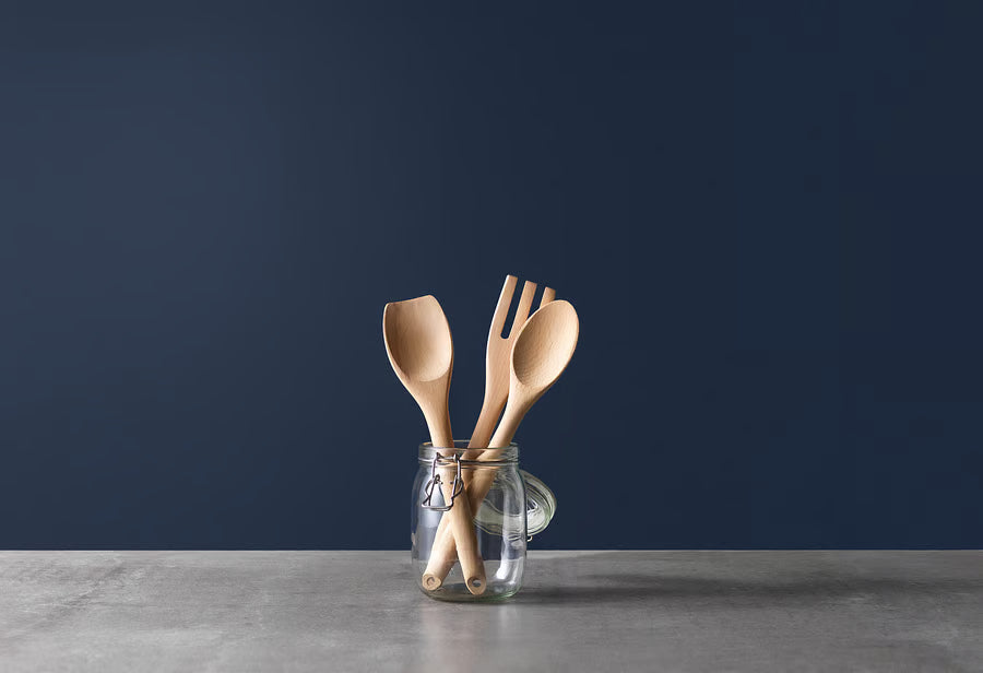 IKEA RÖRT wooden fork alongside spoon and spatula stored upright in a jar against dark blue background