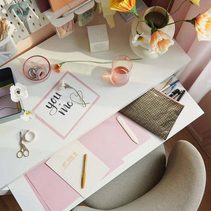 IKEA ROMELSÖN case beside notepads, pens and flowers on a white desk workspace