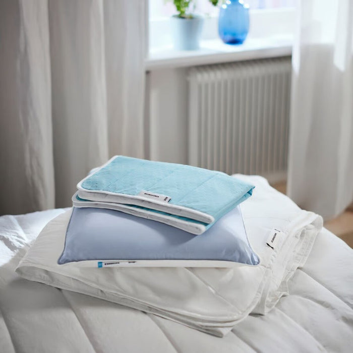Folded blue and white towels on a bed with a window in the background