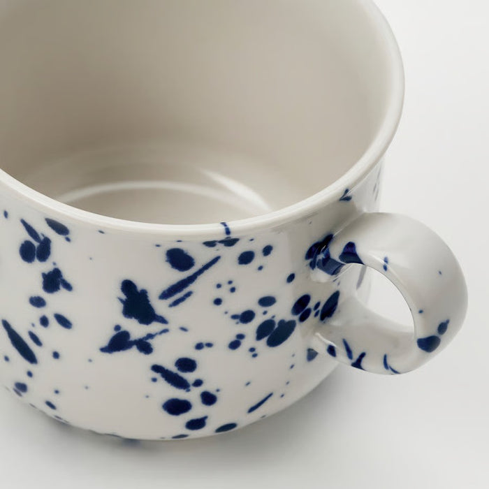 "A ceramic mug with a white base and a pattern of blue splatters and dots, featuring a sturdy handle and a smooth interior, designed for coffee, tea, or other beverages