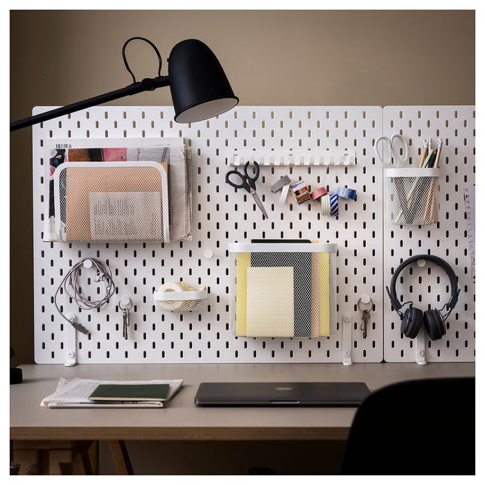 Home desk setup with IKEA SKÅDIS white pegboard mounted using connectors organising office supplies and headphones