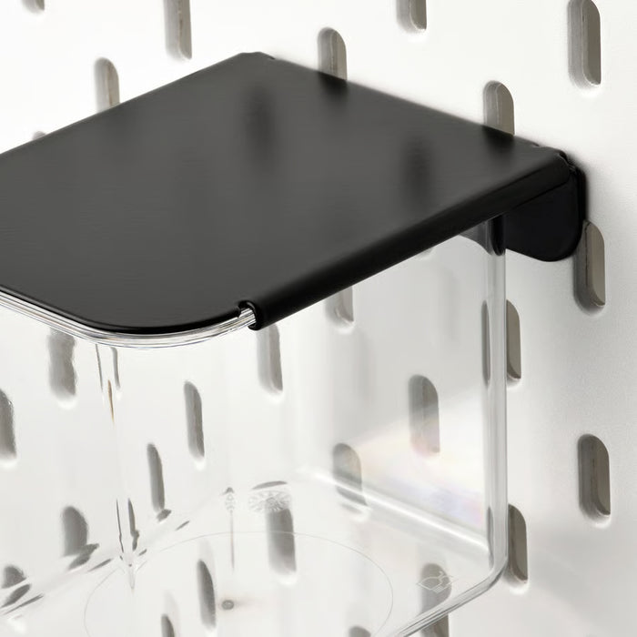 Close-up of IKEA SKÅDIS clear container with black lid mounted on white pegboard