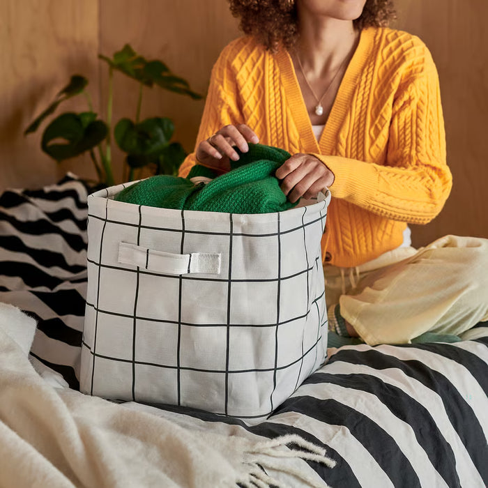 Person organising green towels inside IKEA SLÄTTERVALL basket on bed