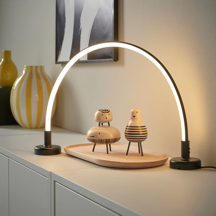 IKEA SMÅSNÖRE curved LED lamp in warm glow on a shelf beside wooden figurines and yellow vases