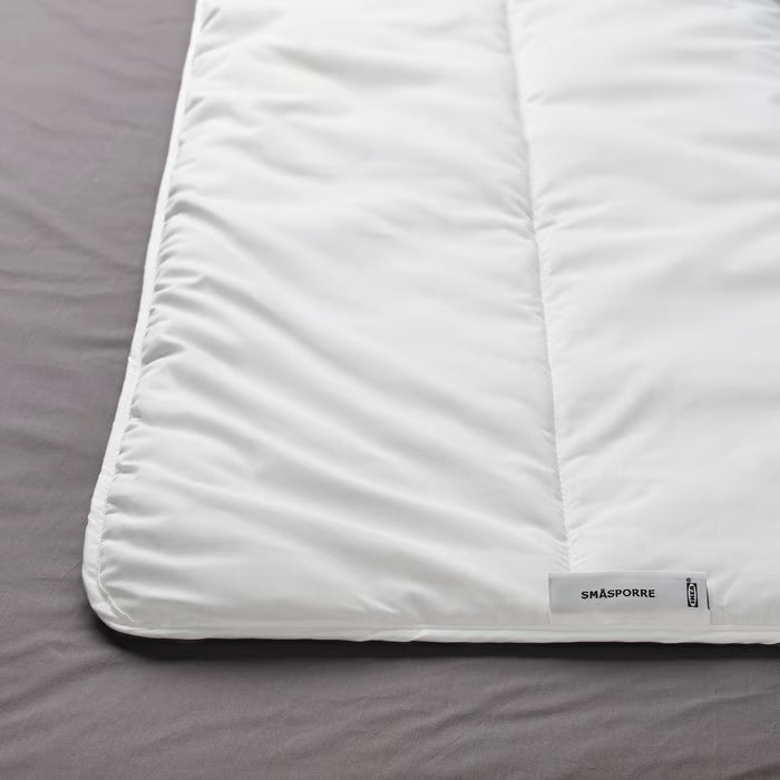 Close-up of IKEA SMÅSPORRE white duvet folded on grey bedsheet showing soft fluffy texture