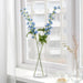 Clear glass vase with blue flowers on a windowsill