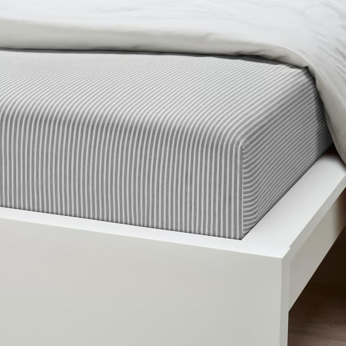 Neatly made bed with IKEA SOLFIBBLA grey striped fitted sheet fitted smoothly over mattress