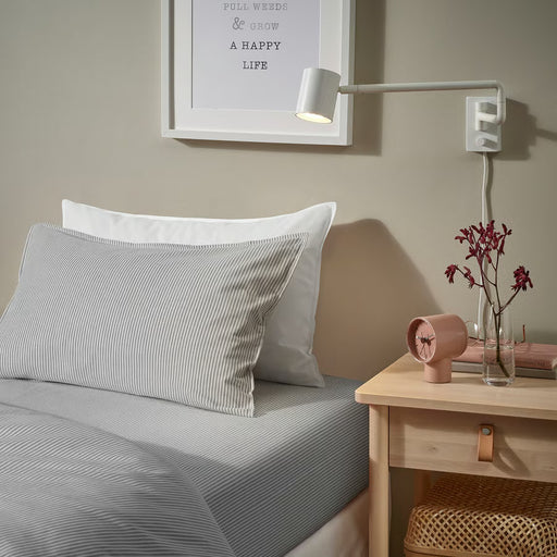 Bed styled with IKEA SOLFIBBLA grey white striped fitted sheet with wooden bedside table and floral decor