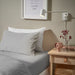  IKEA SOLFIBBLA grey white striped flat sheet styled on bedroom bed with wooden side table and white wall lamp