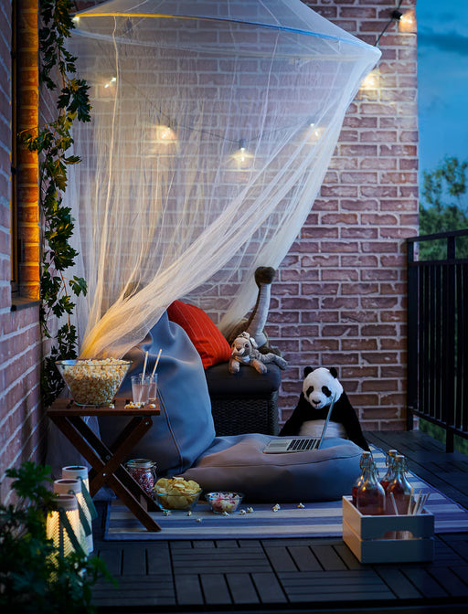 IKEA SOLIG net canopy over outdoor patio seating with cushions and evening string lights