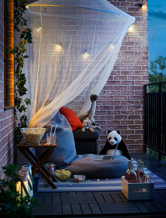 IKEA SOLIG net canopy over outdoor patio seating with cushions and evening string lights
