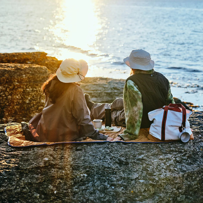 Two people sitting on a rock by the water, enjoying a picnic.