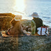 Two people sitting on a rock by the water, enjoying a picnic.