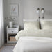 IKEA SORGMANTEL leaf pattern bedding on a minimalist bed with nightstands, dried flowers and wall lamps