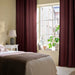 IKEA SPIRBJÖRNBÄR dark maroon curtains on large bedroom window with beige bedding and green plant