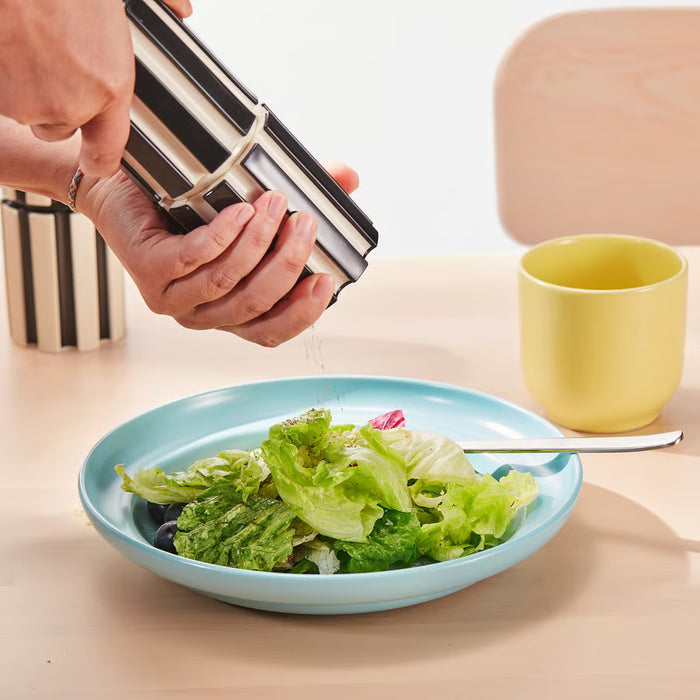 Hand grinding salt with IKEA SPJUTLILJA black and white striped spice mill over fresh salad