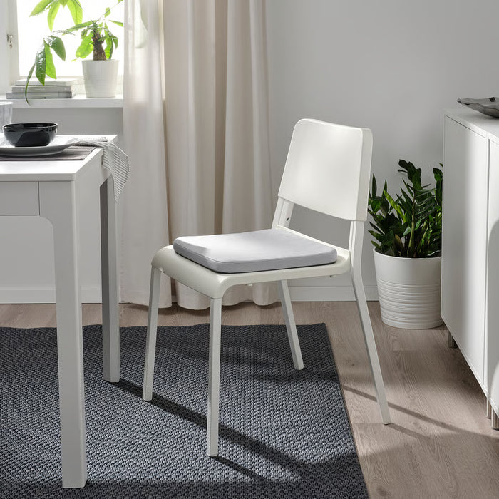 IKEA STAGGSTARR light grey chair pad placed on white dining chair beside a table in minimalist room