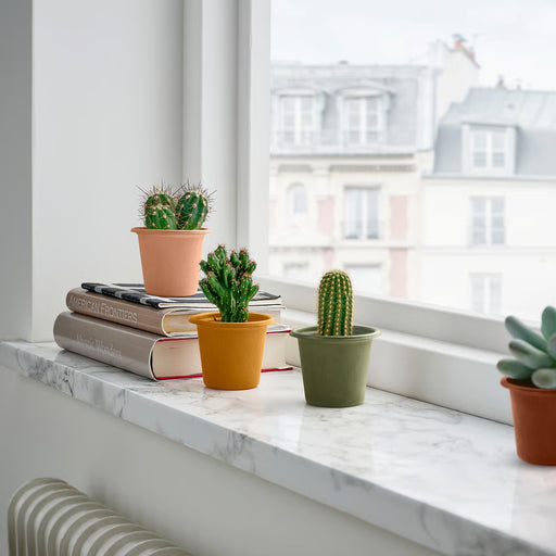IKEA STJÄRNSLINKE colourful plant pots with small cacti on marble windowsill with city view in background