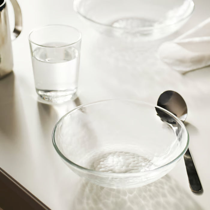 IKEA STRANDKRABBA clear glass bowl with hammered texture beside a spoon and water glass on a table