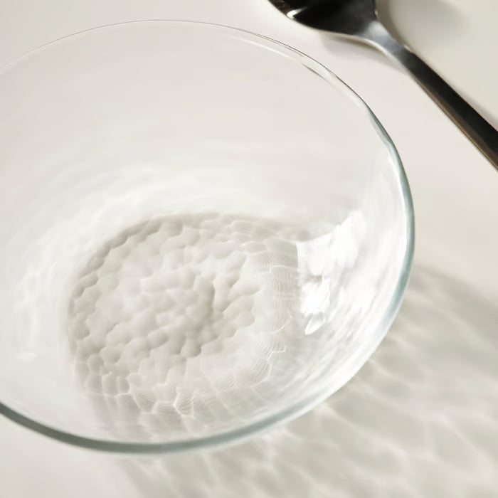Close-up of IKEA STRANDKRABBA ribbed glass bowl casting shadows on a white surface with a spoon