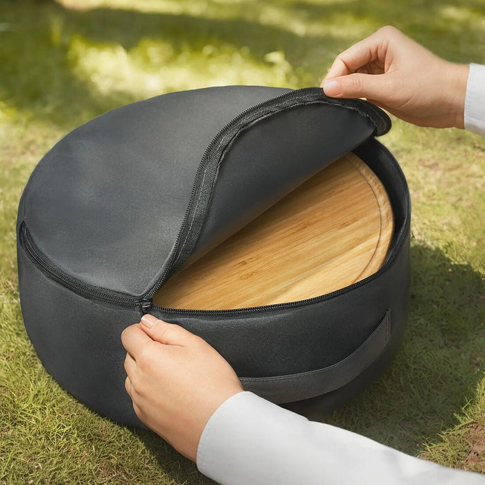 Person opening a black carrying case with a wooden pizza board inside on grass.