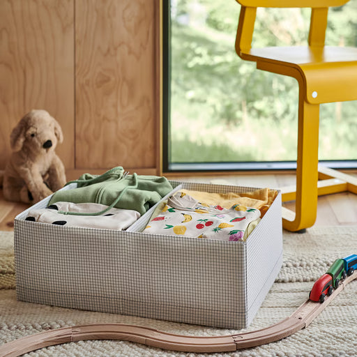 IKEA STUK white black storage box filled with folded clothes placed on rug beside toy train