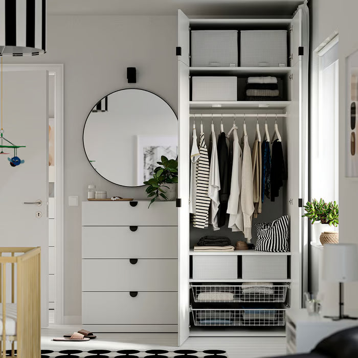 White IKEA wardrobe with STUK boxes folded clothes and mirror beside it in a modern nursery setup