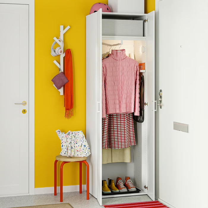 Open closet with IKEA STUK storage box alongside pink sweater skirt and shoes on bright yellow wall