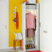 Open closet with IKEA STUK storage box alongside pink sweater skirt and shoes on bright yellow wall
