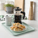 IKEA TILLGÅNG pale green tray holding coffee maker cups and pastries on kitchen counter