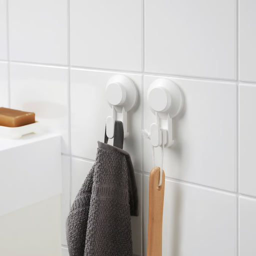 IKEA TISKEN white suction cup hooks holding grey hand towel and wooden spatula on kitchen tiles