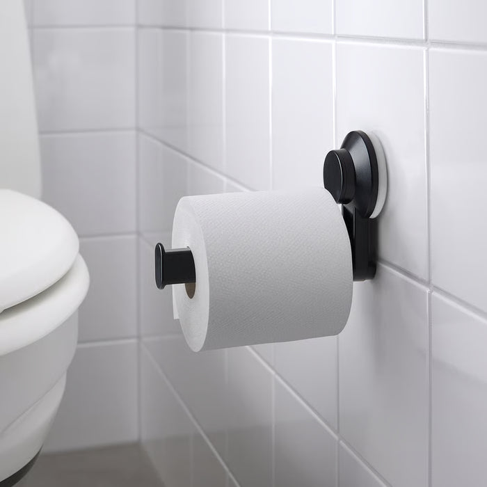 IKEA TISKEN black compact round toilet paper holder with a standard roll, mounted near a white toilet