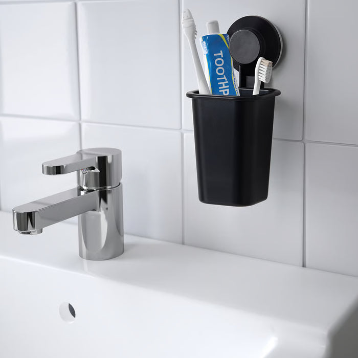 IKEA TISKEN black toothbrush holder mounted near washbasin tap, wall-saving design