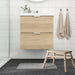 Modern bathroom with IKEA TOFTBO grey-white bath mat placed in front of light wood cabinet and stool