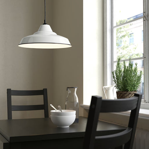 White TRETTIOEN pendant lamp hanging above black dining table near a window with greenery