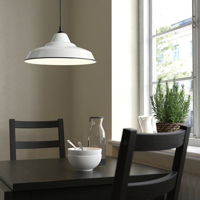 White TRETTIOEN pendant lamp hanging above black dining table near a window with greenery