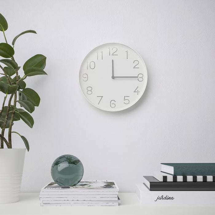IKEA TROMMA white wall clock mounted above a shelf with books, green sphere, and indoor plant