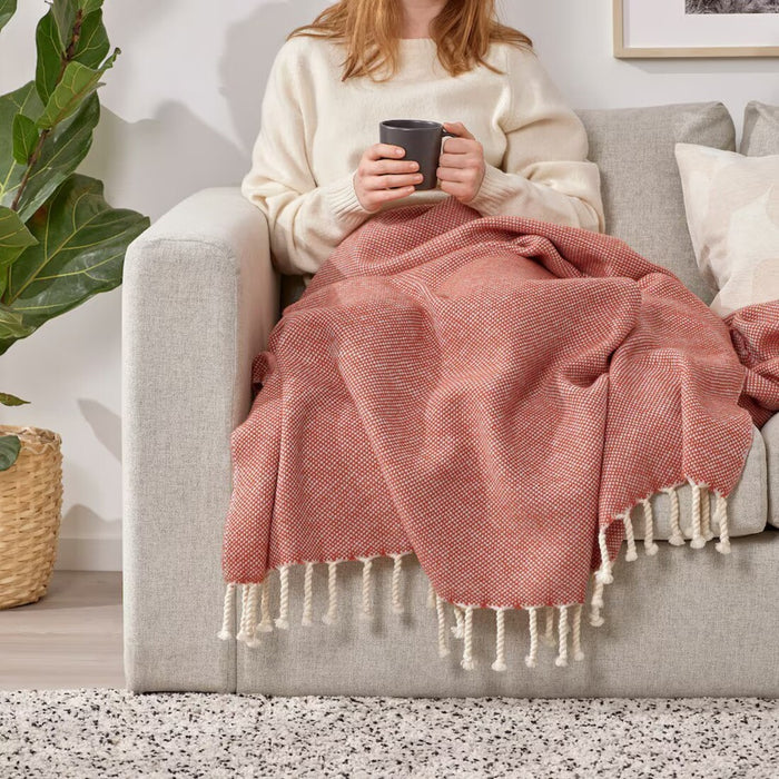 "Woman relaxing on a couch with IKEA ULLTISTEL blush wool throw blanket draped over her lap."