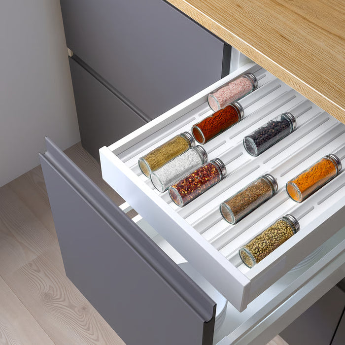 Open kitchen drawer with IKEA UPPDATERA spice rack holding neatly arranged spice jars beside wooden utensils