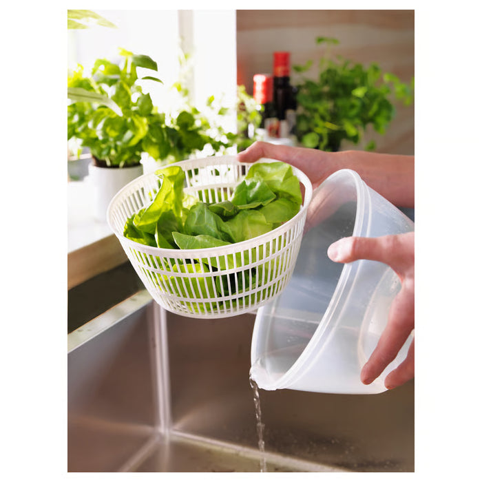 Hand pouring water into IKEA UPPFYLLD white salad spinner with lettuce inside, kitchen sink