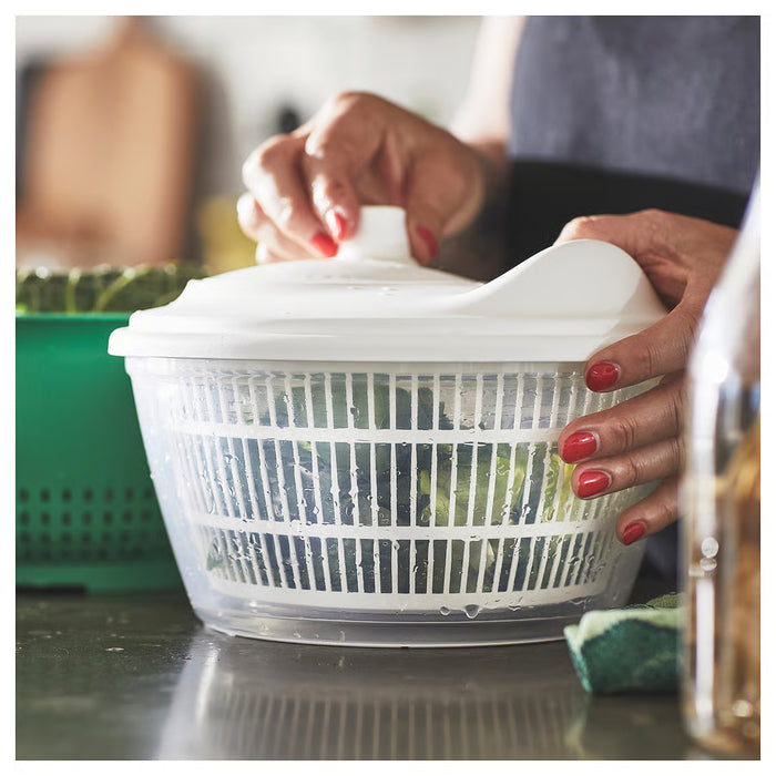 Person with red nail polish using IKEA UPPFYLLD white salad spinner at kitchen sink